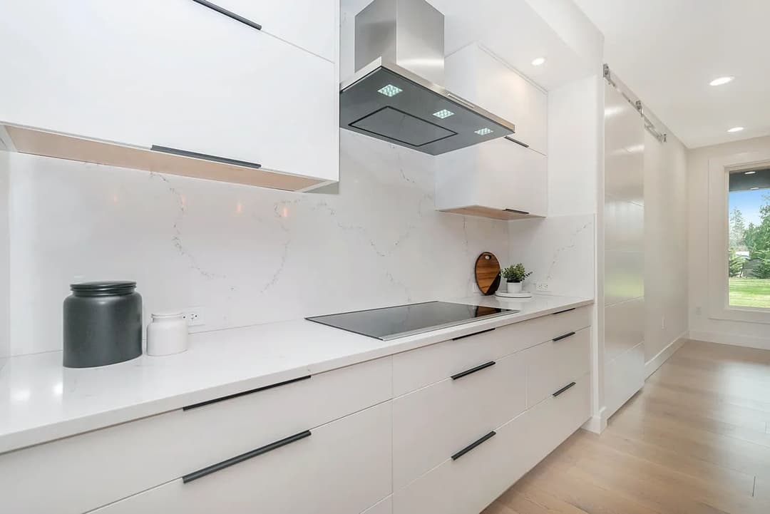 Modern kitchen with white cabinetry, marble backsplash, and sleek appliances.