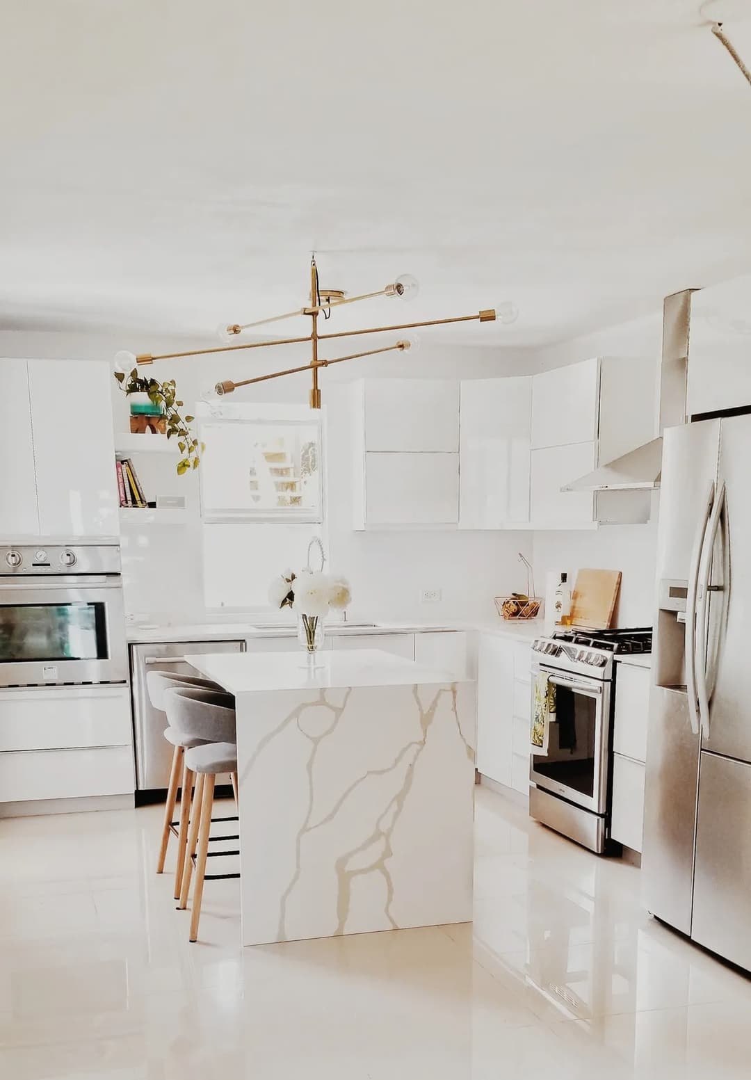 Modern kitchen with white cabinetry, marble island, sleek appliances, and stylish lighting.