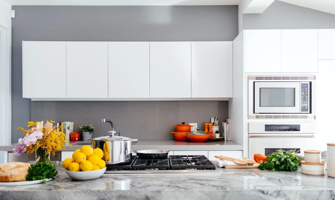 Modern kitchen with white cabinetry, marble countertop, cooking utensils, and fresh produce.
