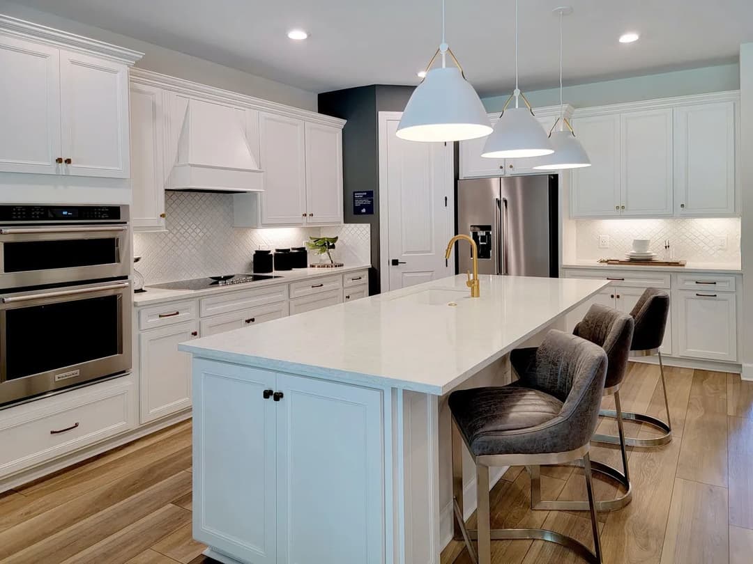 Modern white kitchen with quartz island, stainless steel appliances, and stylish pendant lights.
