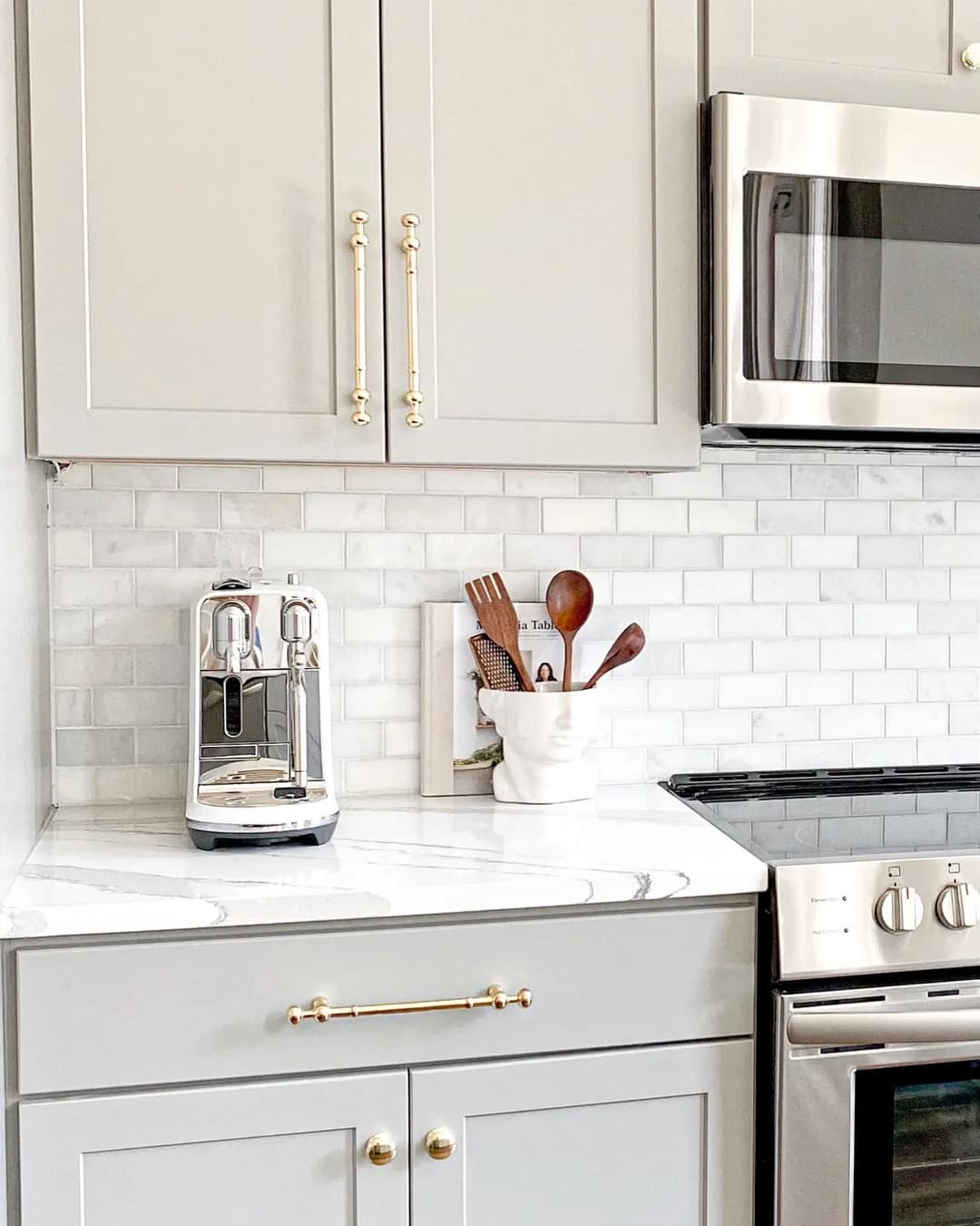 Modern kitchen with gray cabinets, marble countertop, and espresso machine.