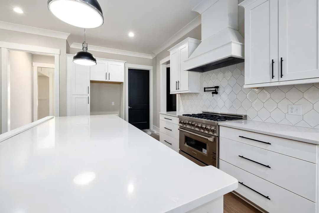 Modern kitchen with white cabinetry, large island, stainless steel appliances, and stylish pendant lights.
