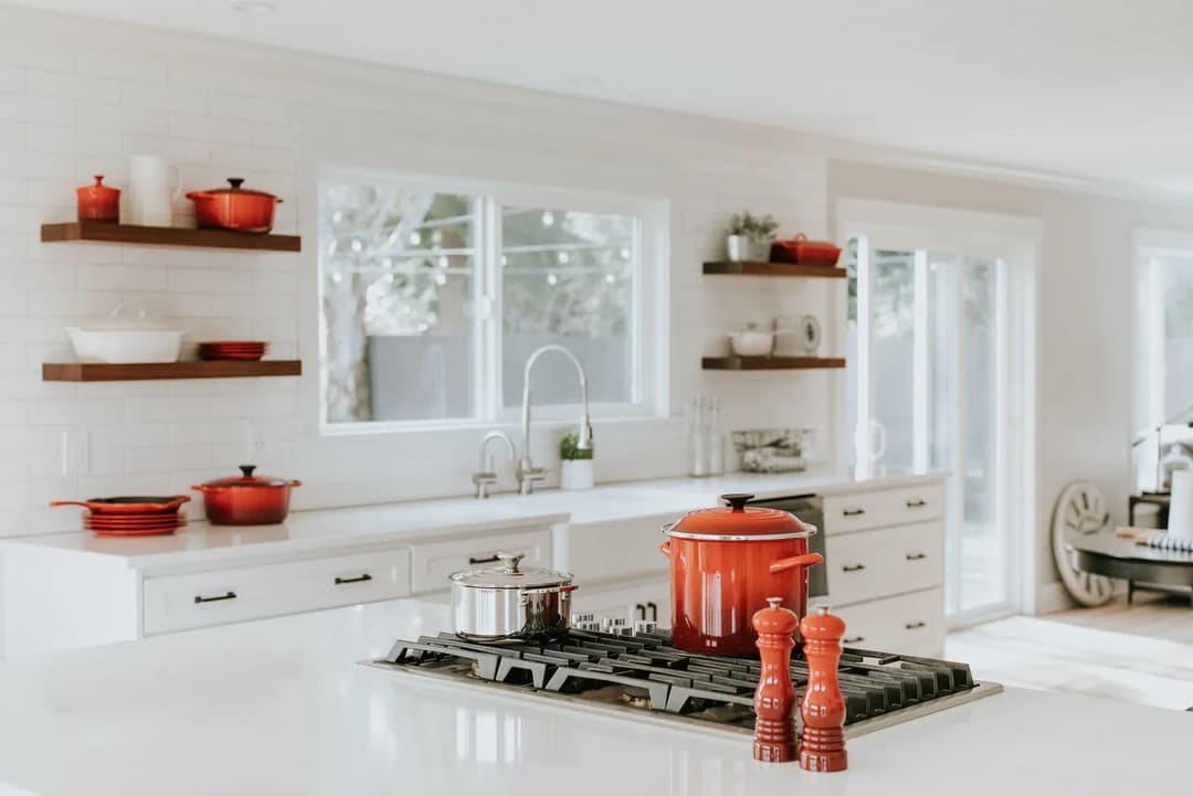 Modern kitchen with red cookware, white cabinetry, and bright natural light.