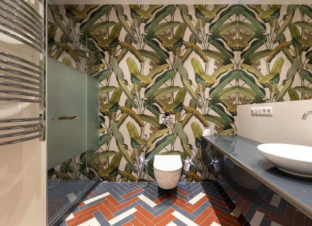 Modern bathroom with tropical leaf wallpaper, white toilet, and stylish patterned floor tiles.
