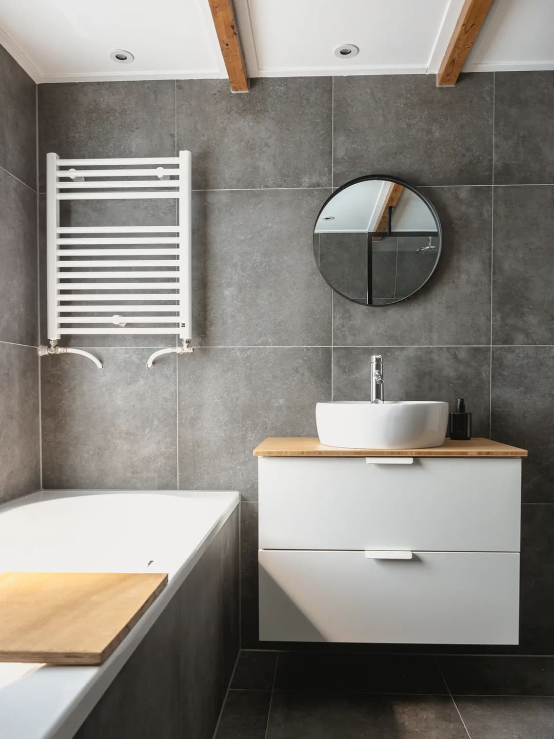 Modern bathroom featuring a round mirror, sleek vanity, bathtub, and heated towel rack.