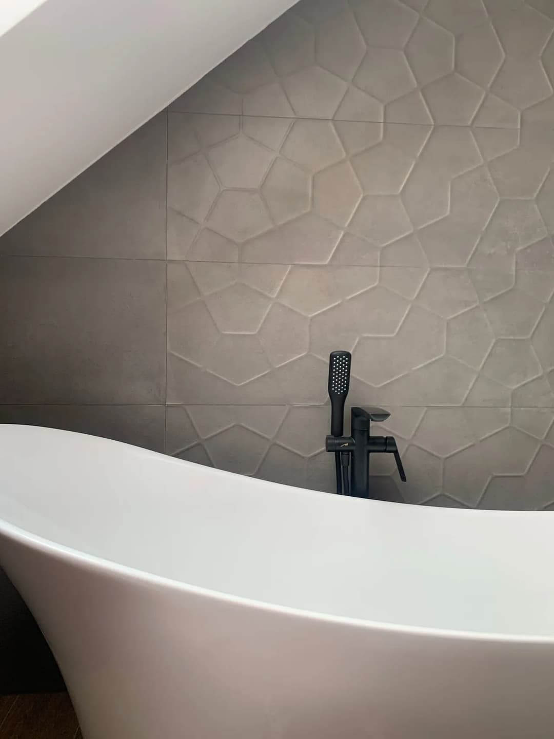 Modern bathroom featuring a sleek freestanding tub and textured gray wall tiles.