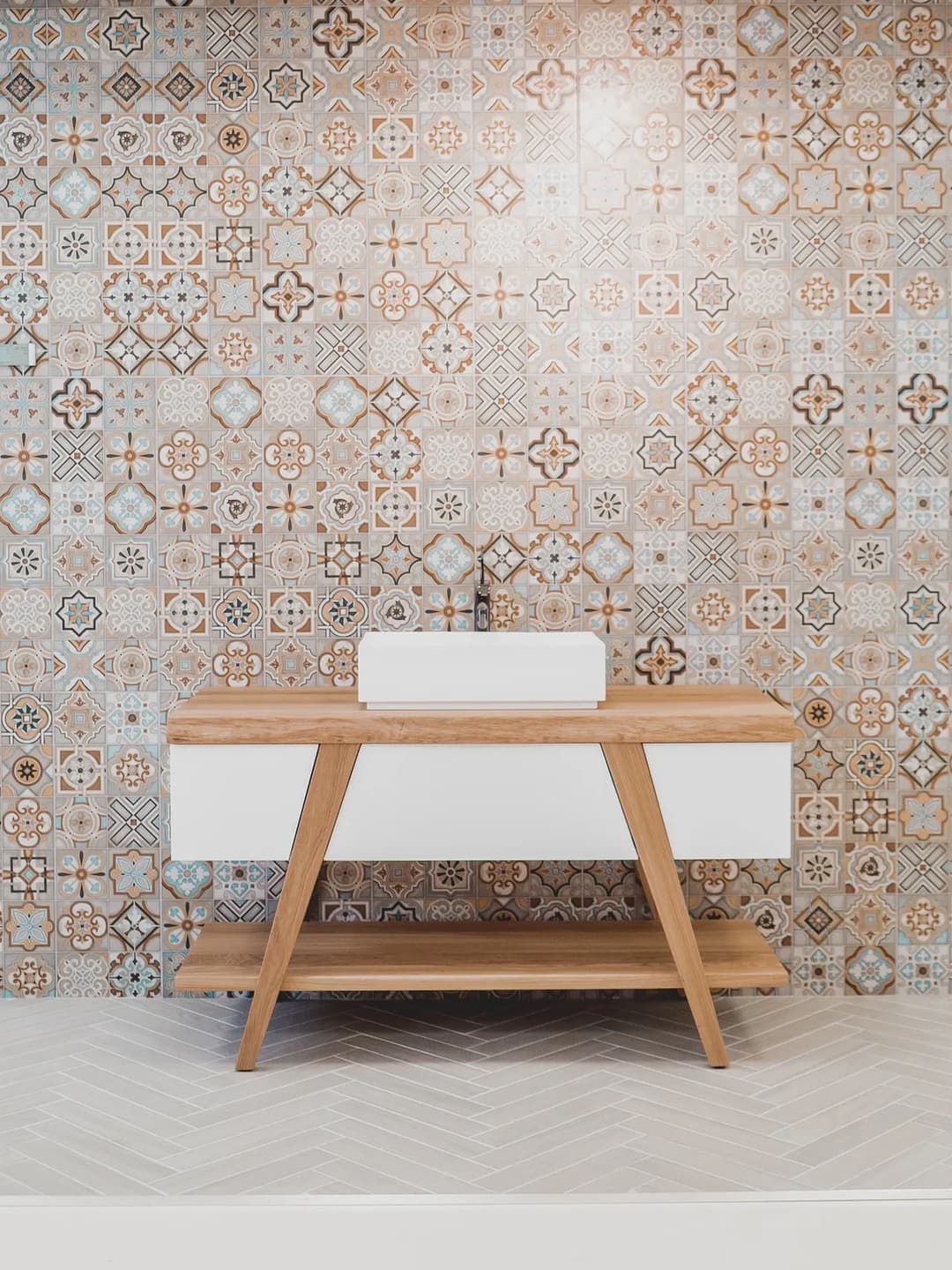 Modern wooden vanity with white sink against intricate patterned tile wall.