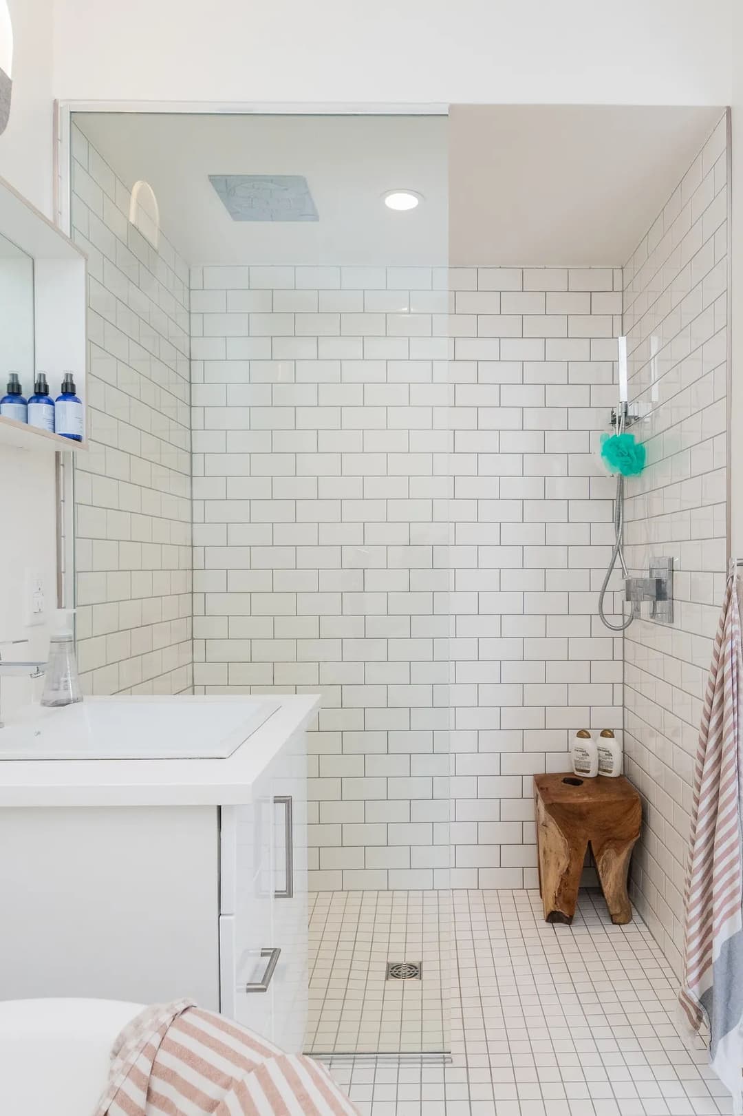 Modern bathroom shower with white subway tiles, wooden stool, and stylish fixtures.