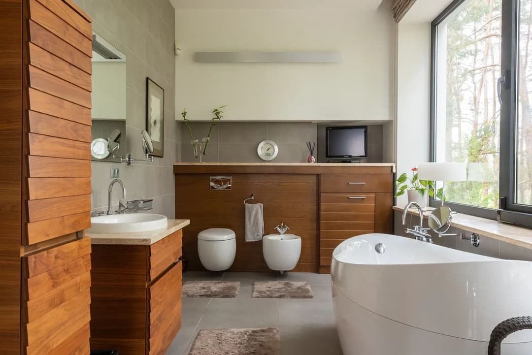 Modern bathroom design featuring a freestanding tub, wooden cabinetry, and large windows.