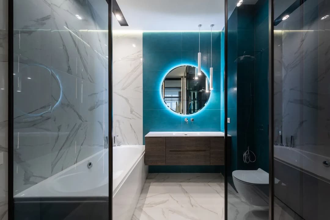 Modern bathroom featuring a round mirror, glass shower, and marble accents. Sleek design.