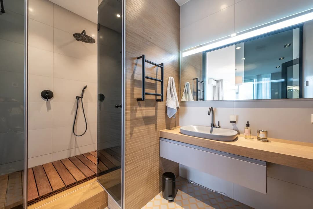 Modern bathroom with walk-in shower, wood accents, sleek vanity, and stylish lighting.