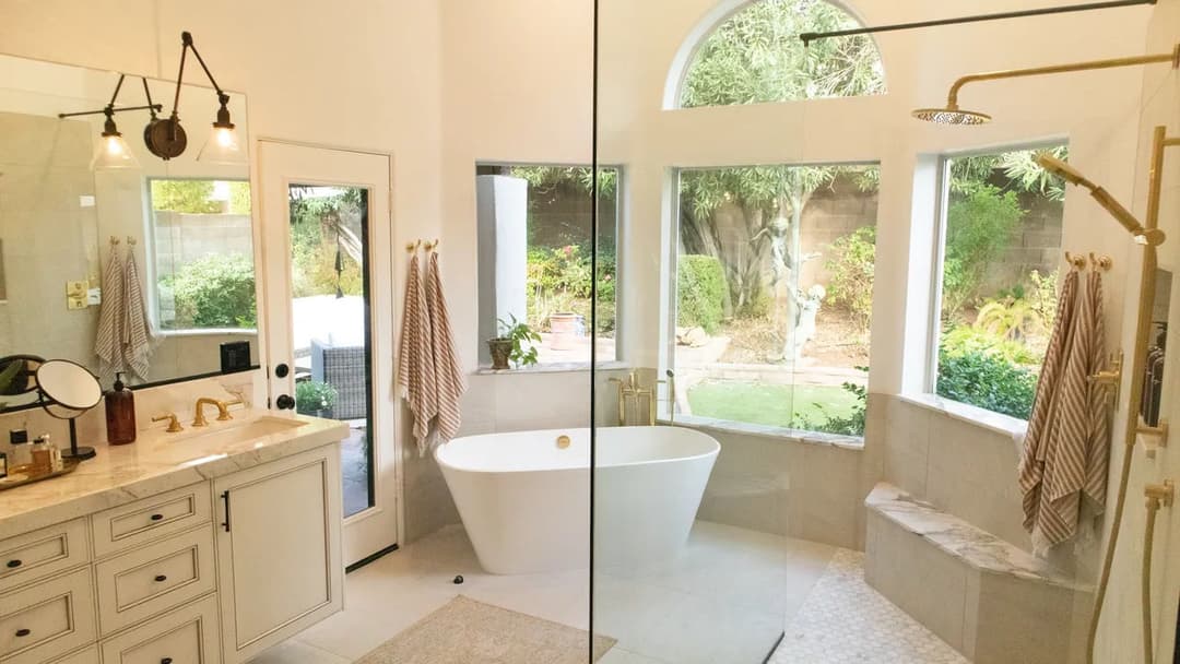 Spacious modern bathroom with a freestanding tub, glass shower, and lush garden view.