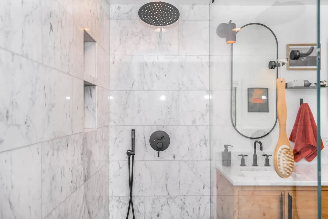 Modern marble shower with rainfall showerhead, sleek fixtures, and wooden bath accessories.