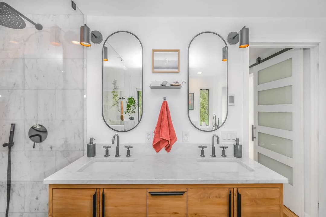 Modern bathroom with dual mirrors, marble countertop, and stylish fixtures in a light setting.