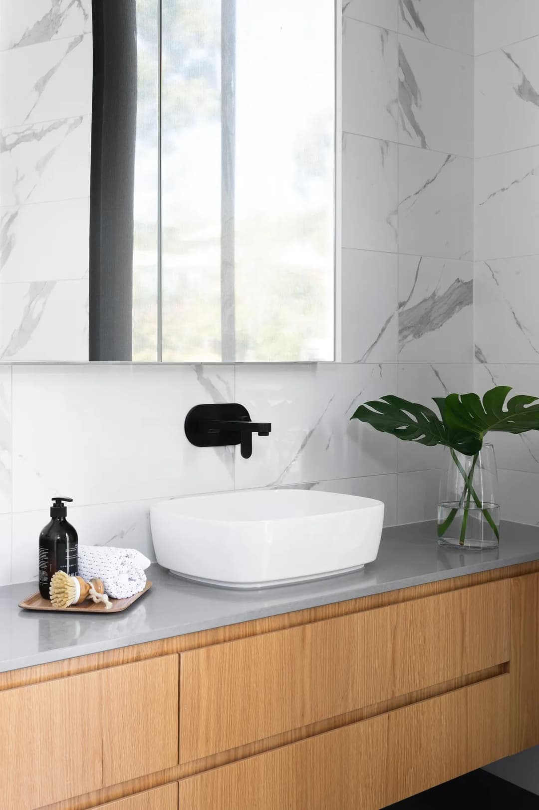 Modern bathroom featuring a sleek white sink, black faucet, and natural wood cabinetry.