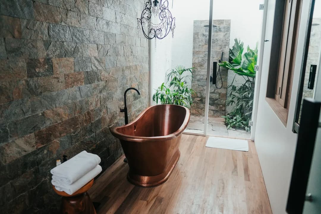 Copper bathtub in a modern bathroom with stone walls and greenery outside. Elegant decor.