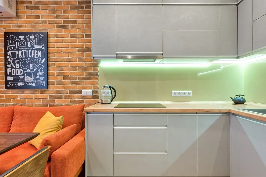 Modern kitchen with gray cabinetry, wooden countertop, orange sofa, and stylish wall art.