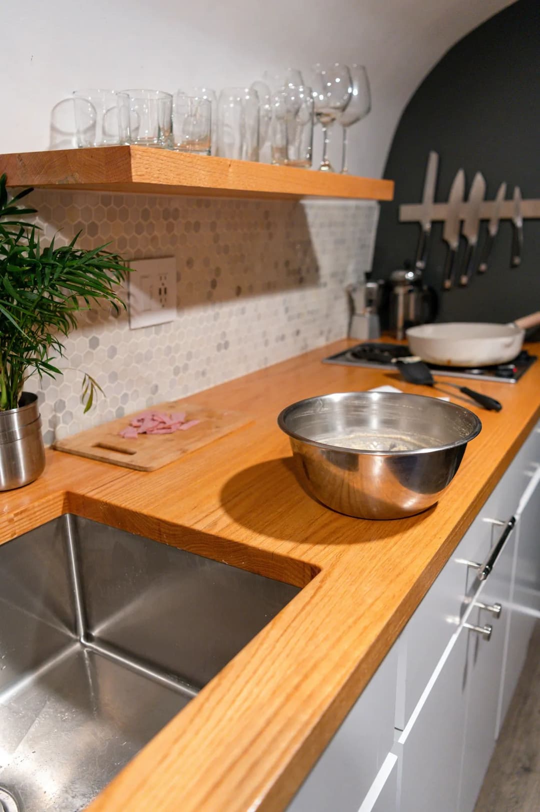 Modern kitchen countertop with stainless steel sink, cooking utensils, and glassware.