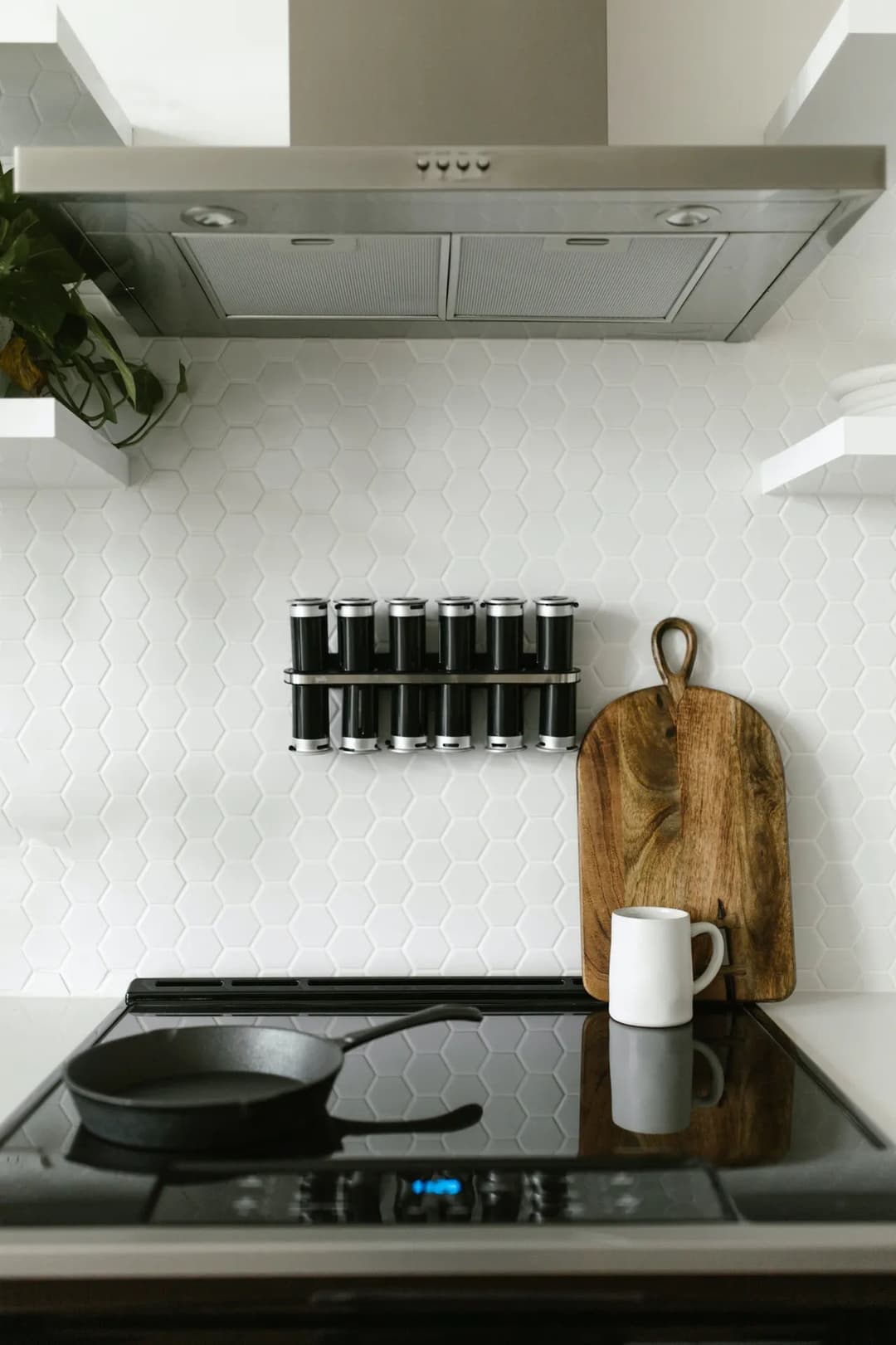 Modern kitchen with hexagon tiles, spice rack, wooden cutting board, and white mug on stove.