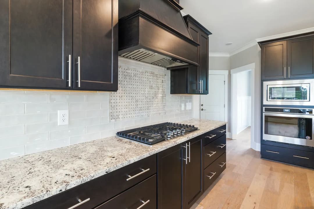 Modern kitchen with dark cabinets, granite countertop, gas stove, and mosaic backsplash.