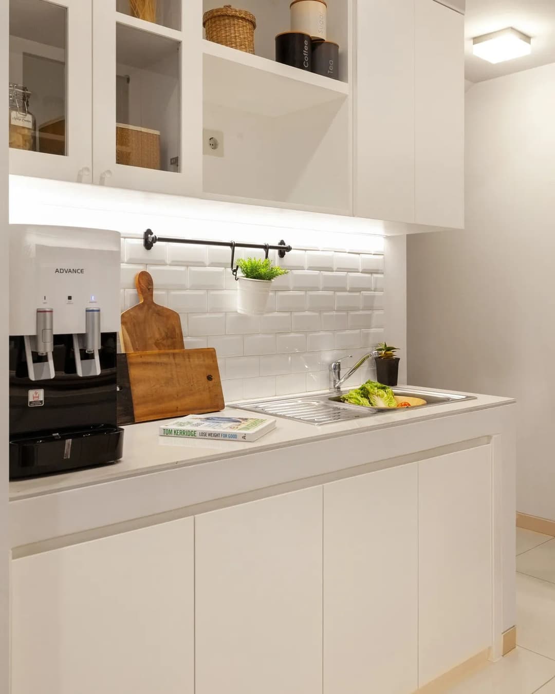 Modern kitchen with white cabinets, water dispenser, wooden cutting board, and sink with vegetables.