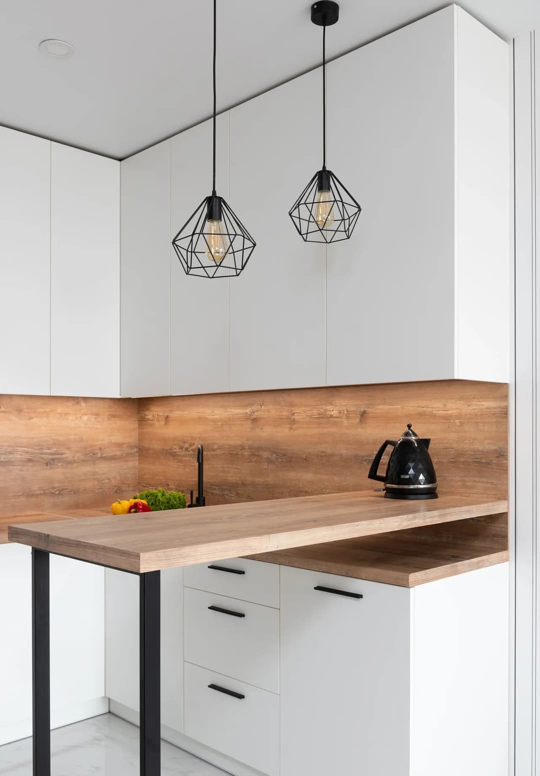 Modern kitchen with white cabinets, wooden accents, black pendant lights, and a kettle.