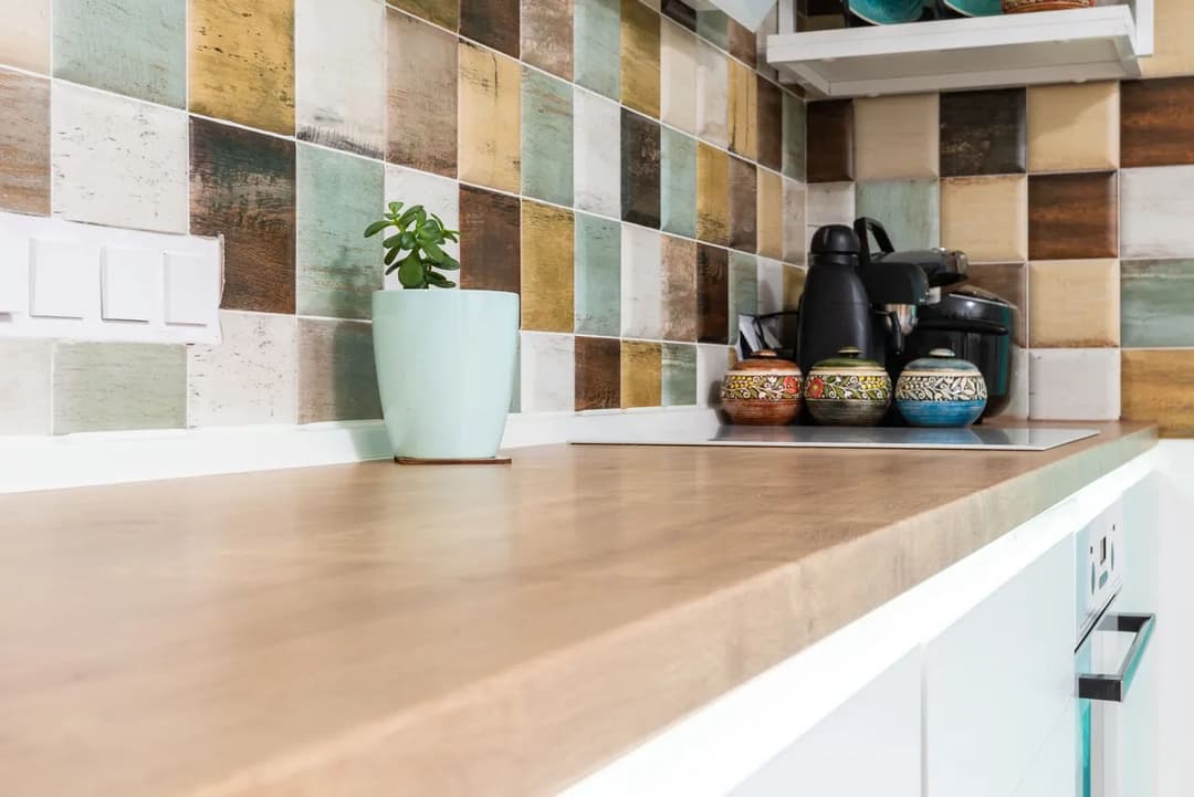 Modern kitchen counter with colorful tiled backsplash, coffee maker, and potted plant.