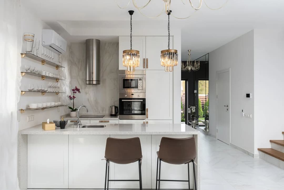 Modern kitchen with white cabinetry, elegant lighting, and minimalist decor. Stylish bar stools included.