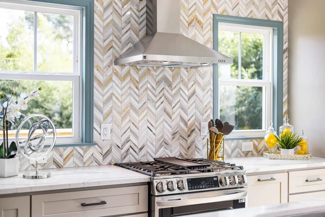 Modern kitchen with herringbone tile backsplash, stainless steel hood, and gas range.