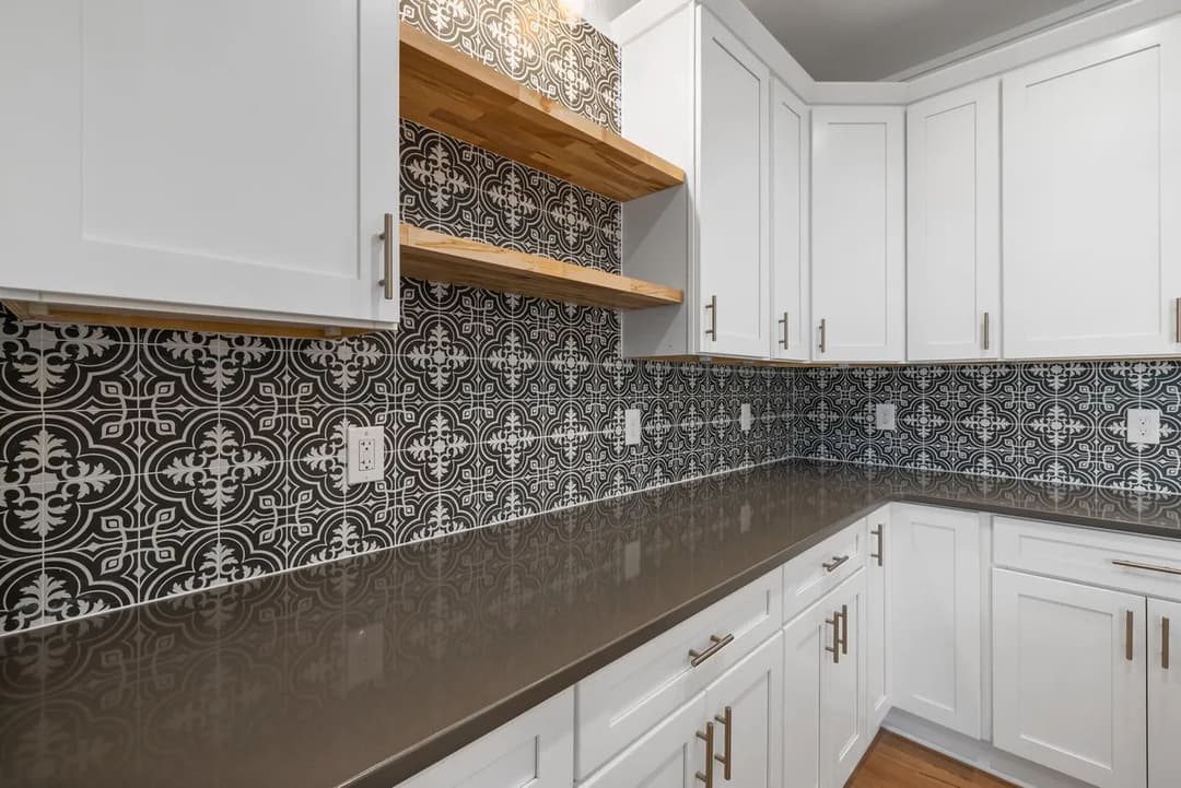 Modern kitchen with white cabinets, patterned backsplash, and wooden open shelves.