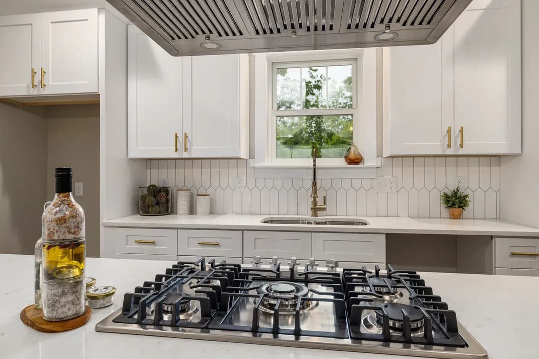 Modern kitchen with gas stove, marble countertops, white cabinets, and natural light.