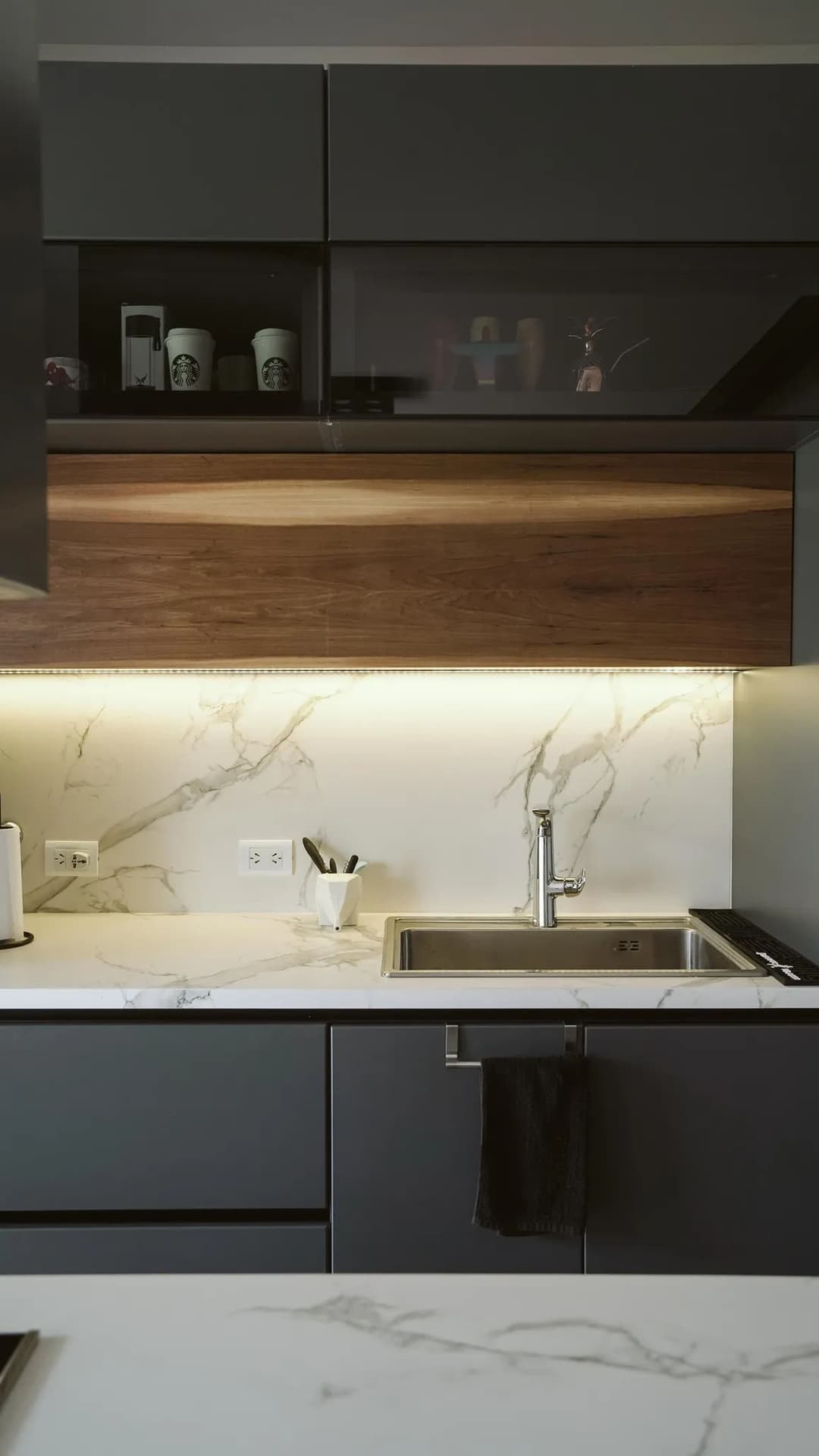 Modern kitchen featuring dark cabinetry, marble countertops, and under-cabinet lighting.