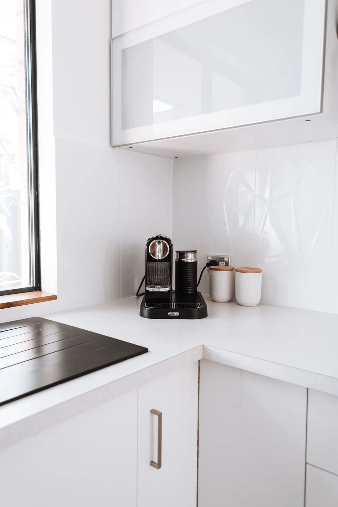 Modern kitchen corner featuring a black espresso machine, white cabinets, and clean surfaces.