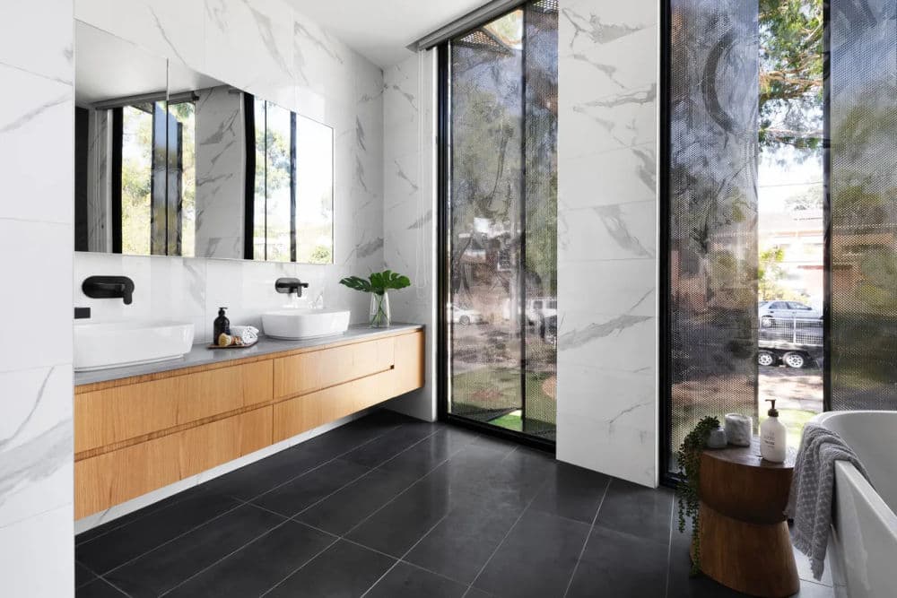 Modern bathroom with marble walls, wood cabinetry, large windows, and sleek fixtures.
