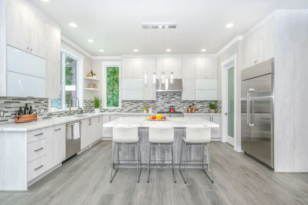 Modern kitchen with white cabinetry, grey backsplash, and an island with bar stools.